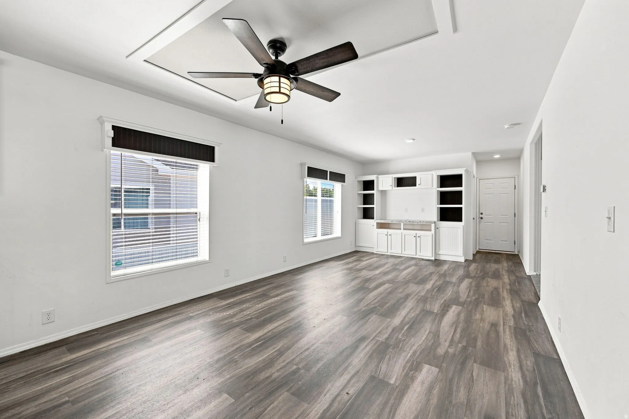 Wood-finish flooring, recessed ceiling detail, ceiling fan with integrated lighting, built-in cabinetry, and crisp white walls