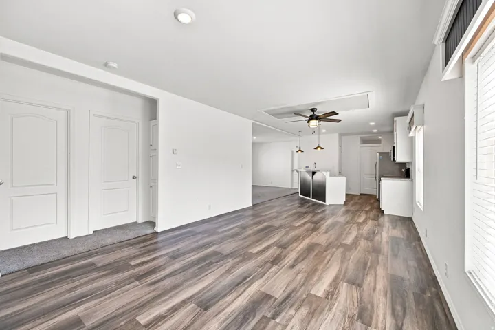 Wood-finish flooring throughout, recessed ceiling lighting, kitchen island with pendant lighting, white cabinetry, and stainless steel refrigerator