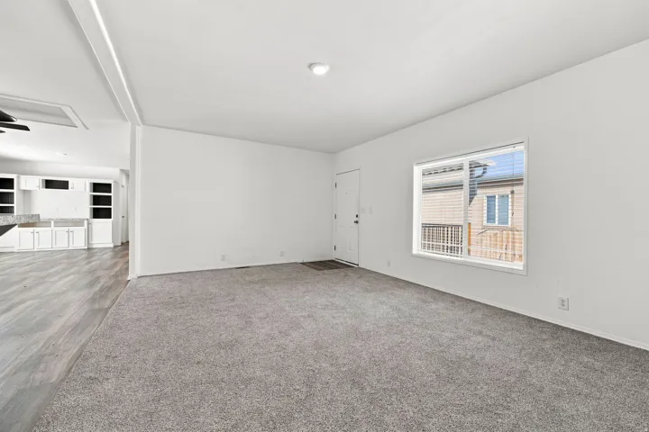 Spacious living area with grey carpeting, white walls, recessed lighting, and a front entry door