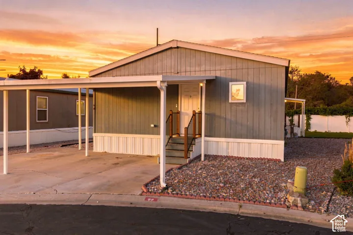 Exterior siding, covered carport, gravel landscaping, front entry porch with steps, and a white perimeter fence