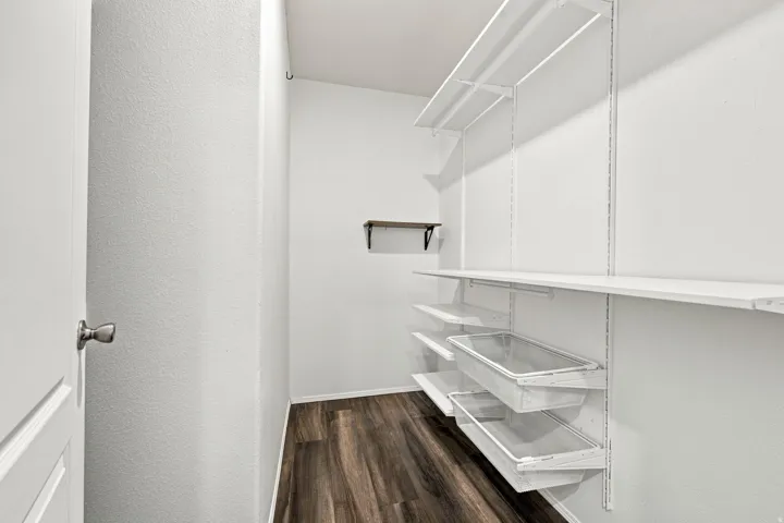 Wood-finish flooring, white walls, built-in shelving system, sliding storage bins, and a wall-mounted floating shelf