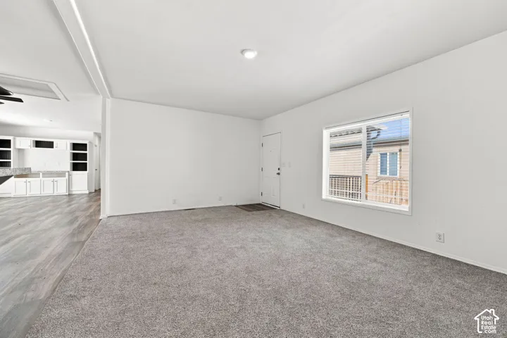 Spacious living area with grey carpeting, white walls, recessed lighting, and a front entry door
