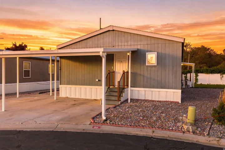 Exterior siding, covered carport, gravel landscaping, front entry porch with steps, and a white perimeter fence