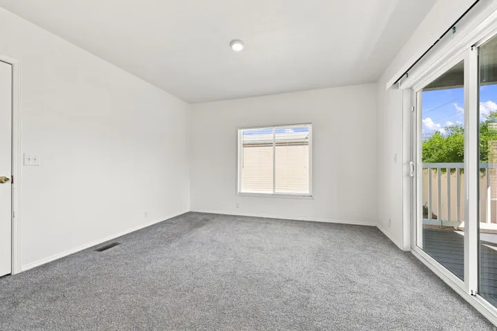 Plush carpeting, a large window, and sliding glass doors to the exterior balcony