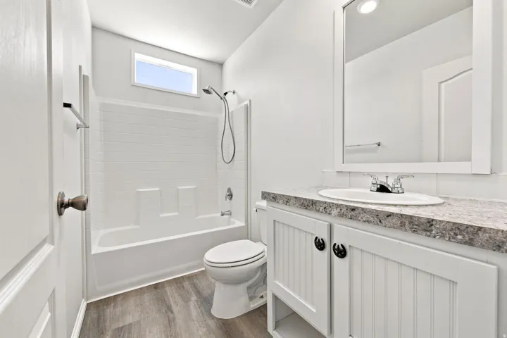 Spa-inspired bathroom featuring a frameless glass-enclosed shower with subway tile surround, dual vanity with quartz countertop and brushed nickel hardware, porcelain toilet, and wood-finish flooring throughout