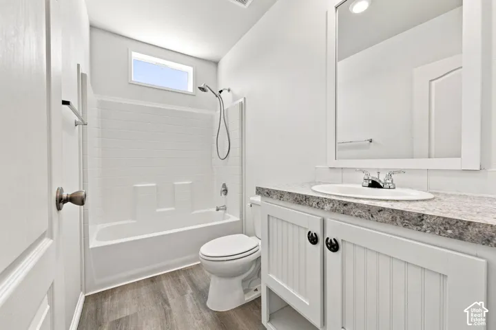 Spa-inspired bathroom featuring a frameless glass-enclosed shower with subway tile surround, dual vanity with quartz countertop and brushed nickel hardware, porcelain toilet, and wood-finish flooring throughout