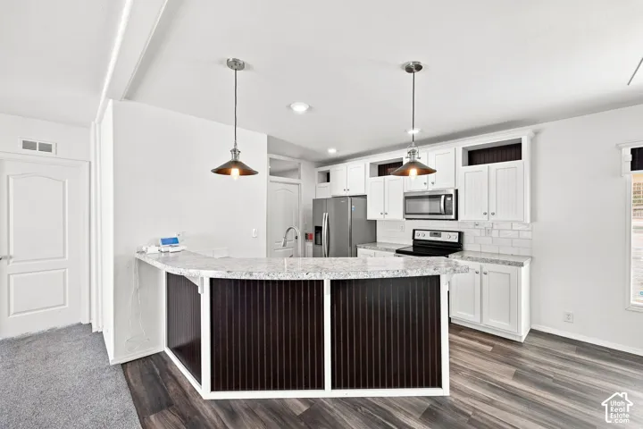 Modern kitchen featuring a breakfast bar with pendant lighting, white cabinetry, integrated stainless steel appliances, and wood-finish flooring