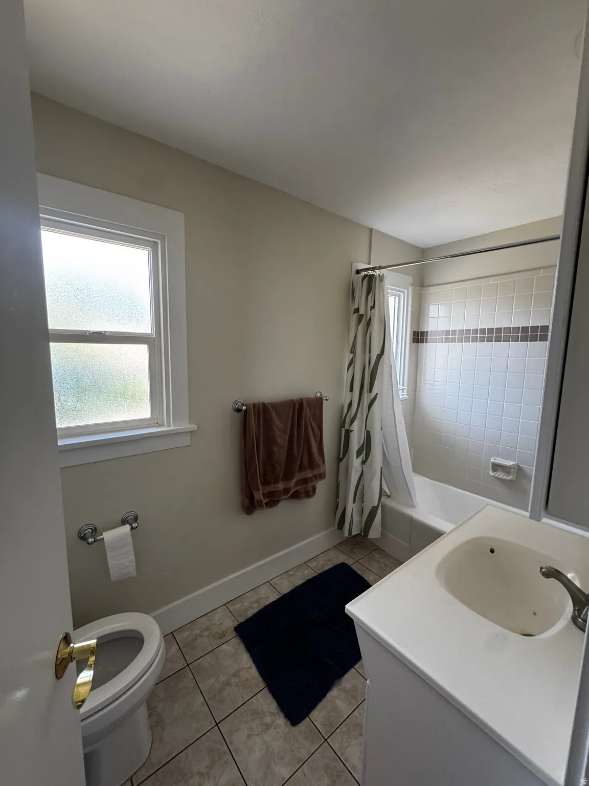 Bathroom with ceramic tile flooring, a white vanity with integrated sink, a built-in bathtub with subway tile surround, and a window with frosted glass