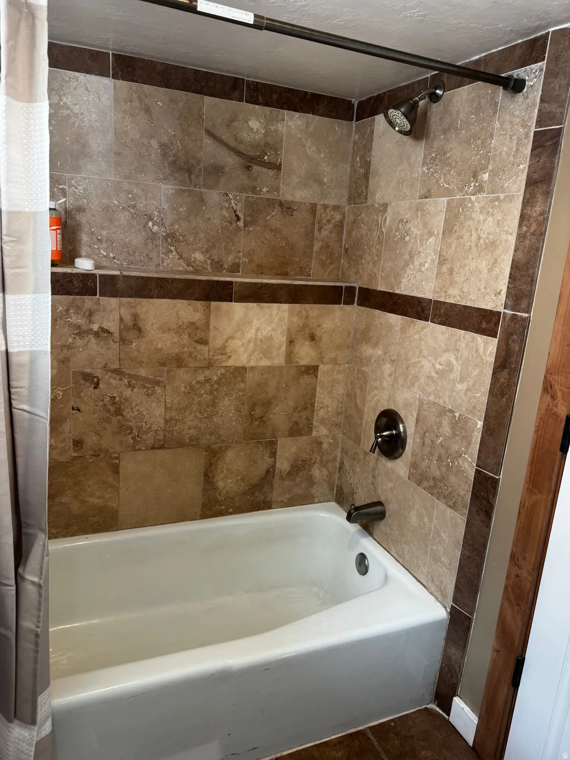 Bathtub with tiled surround featuring an accent border, built-in shelving, and a shower head