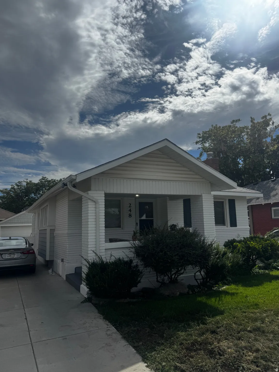 White siding exterior featuring a covered front porch, dark shutters, and a well-defined driveway