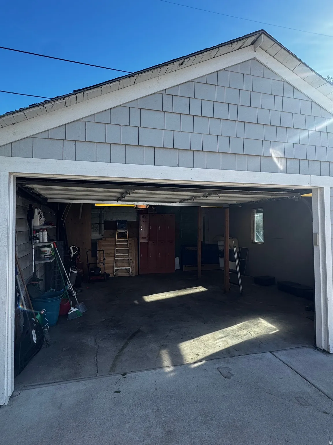 Gabled exterior with shingle siding, an open garage door, and a concrete floor