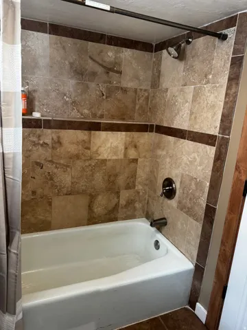 Bathtub with tiled surround featuring an accent border, built-in shelving, and a shower head