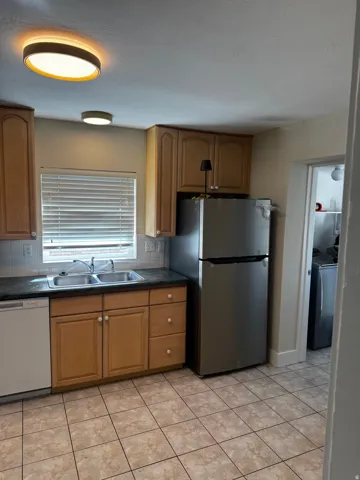 Kitchen featuring wood-finish cabinetry, stainless steel refrigerator, white dishwasher, and tiled flooring