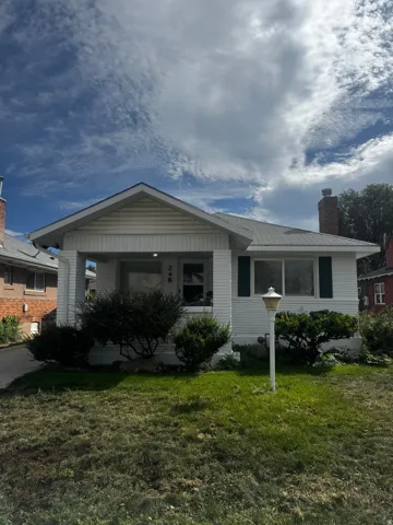 White siding exterior with a pitched roof, front porch, and brick chimney
