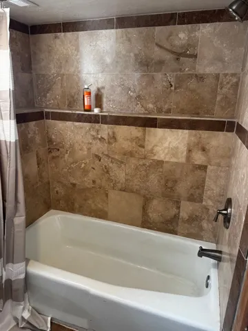 Bathtub with a shower head, tiled surround, integrated shelf, and dark trim accents
