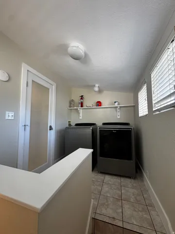 Laundry area featuring tiled flooring, a built-in shelving unit, and multiple windows with blinds