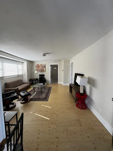 Light wood-finish flooring throughout, featuring a window with horizontal blinds and a doorway with white trim