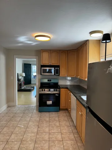 Kitchen featuring tile flooring, wood-finish cabinetry, stainless steel appliances, and a dark countertop