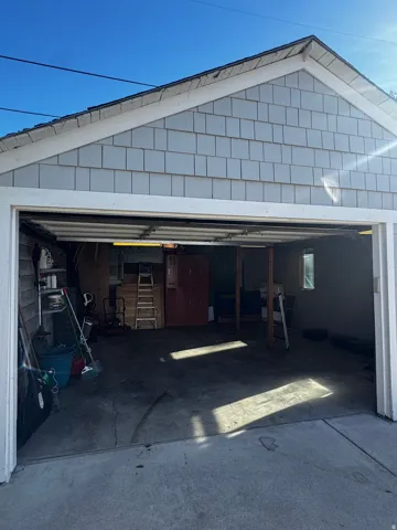 Gabled exterior with shingle siding, an open garage door, and a concrete floor