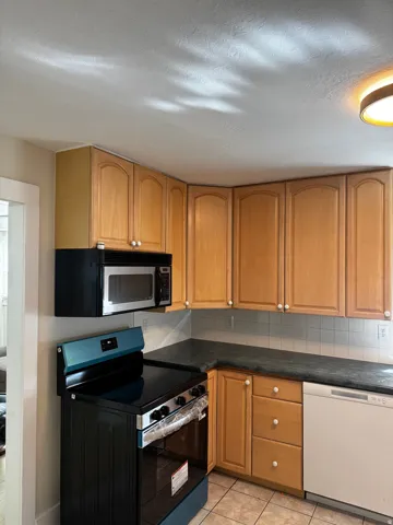 Neutral-toned kitchen cabinetry with integrated microwave, tile flooring, and dark countertops