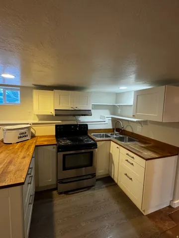 U-shaped kitchen with wood-finish countertops, white shaker-style cabinetry, stainless steel range, and dual stainless steel sink