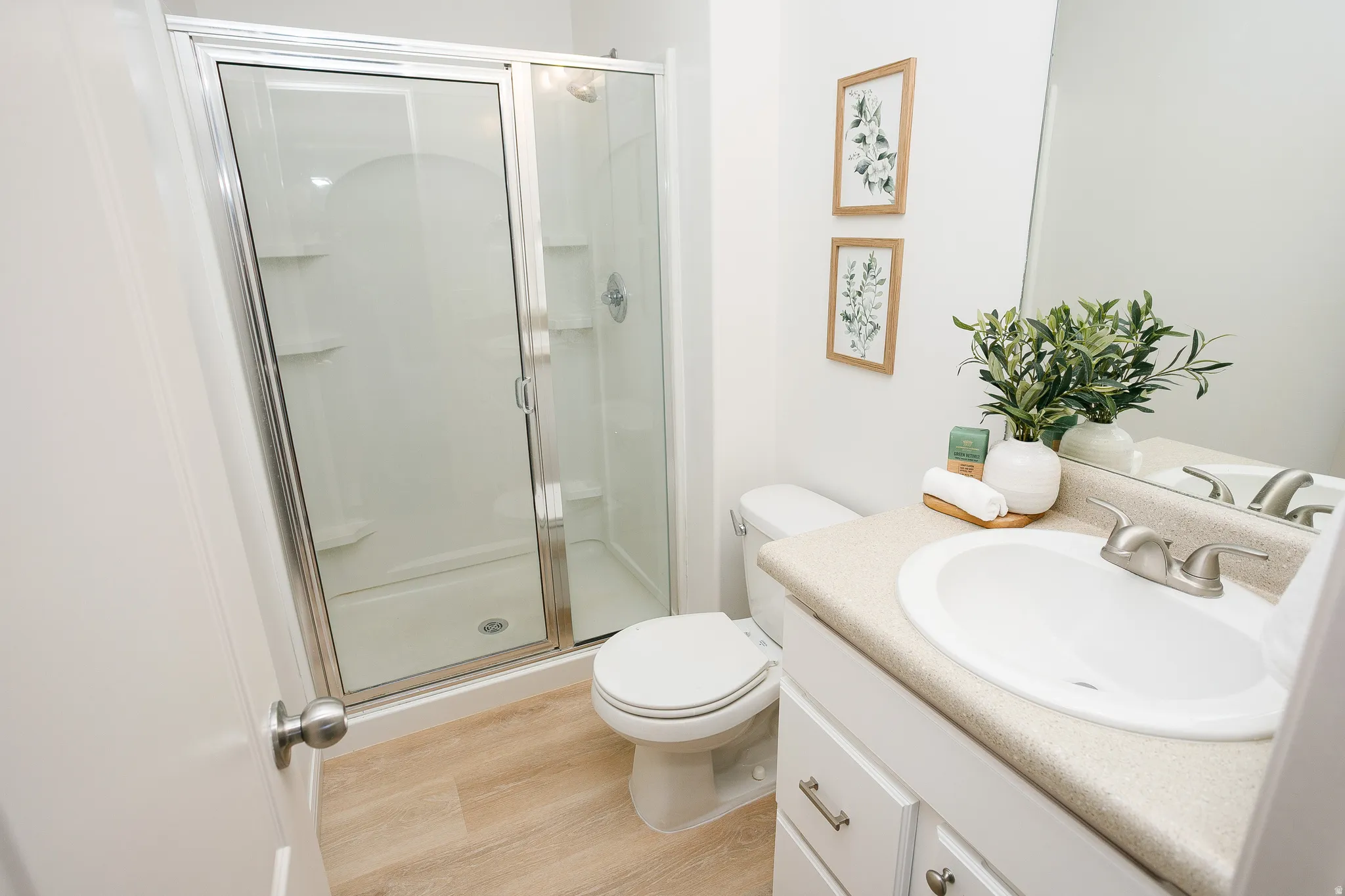 Walk-in shower with sliding glass door, single vanity with integrated sink, light-toned countertop, and wood-finish flooring