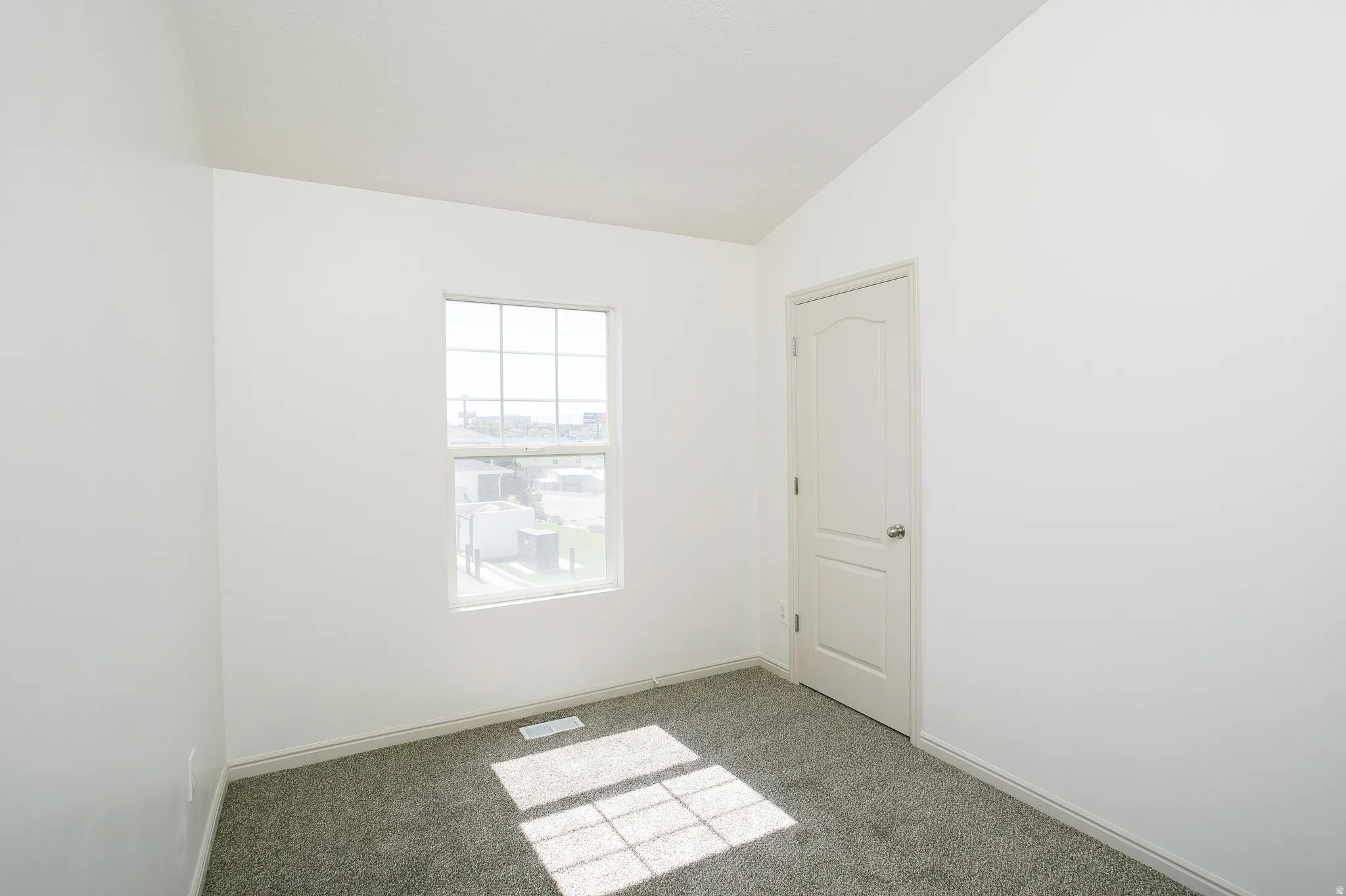 Carpeted flooring, white interior door, window with grid, white walls, vaulted ceiling