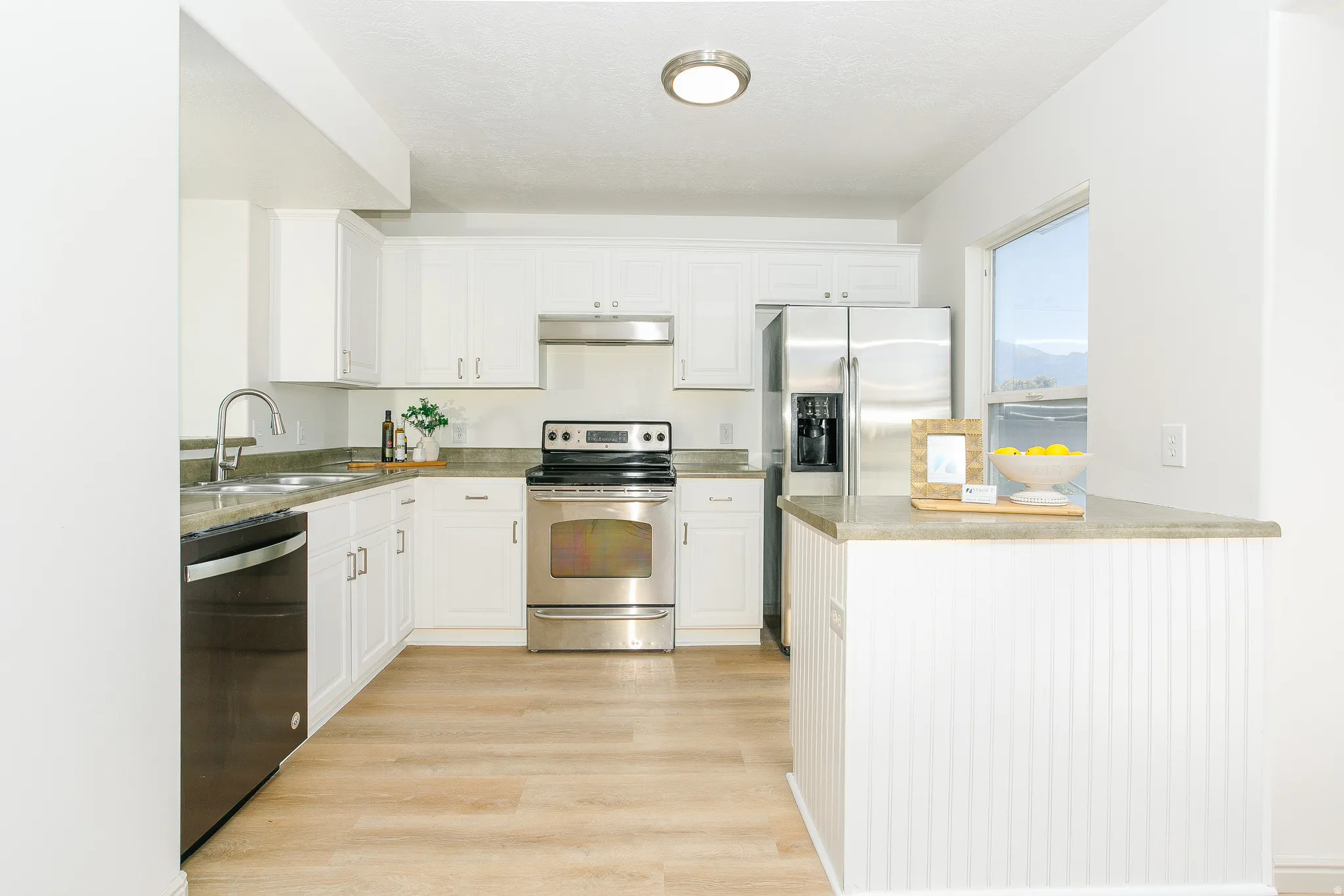 White cabinetry, stainless steel appliances, wood-finish flooring, and a breakfast bar with a solid surface countertop