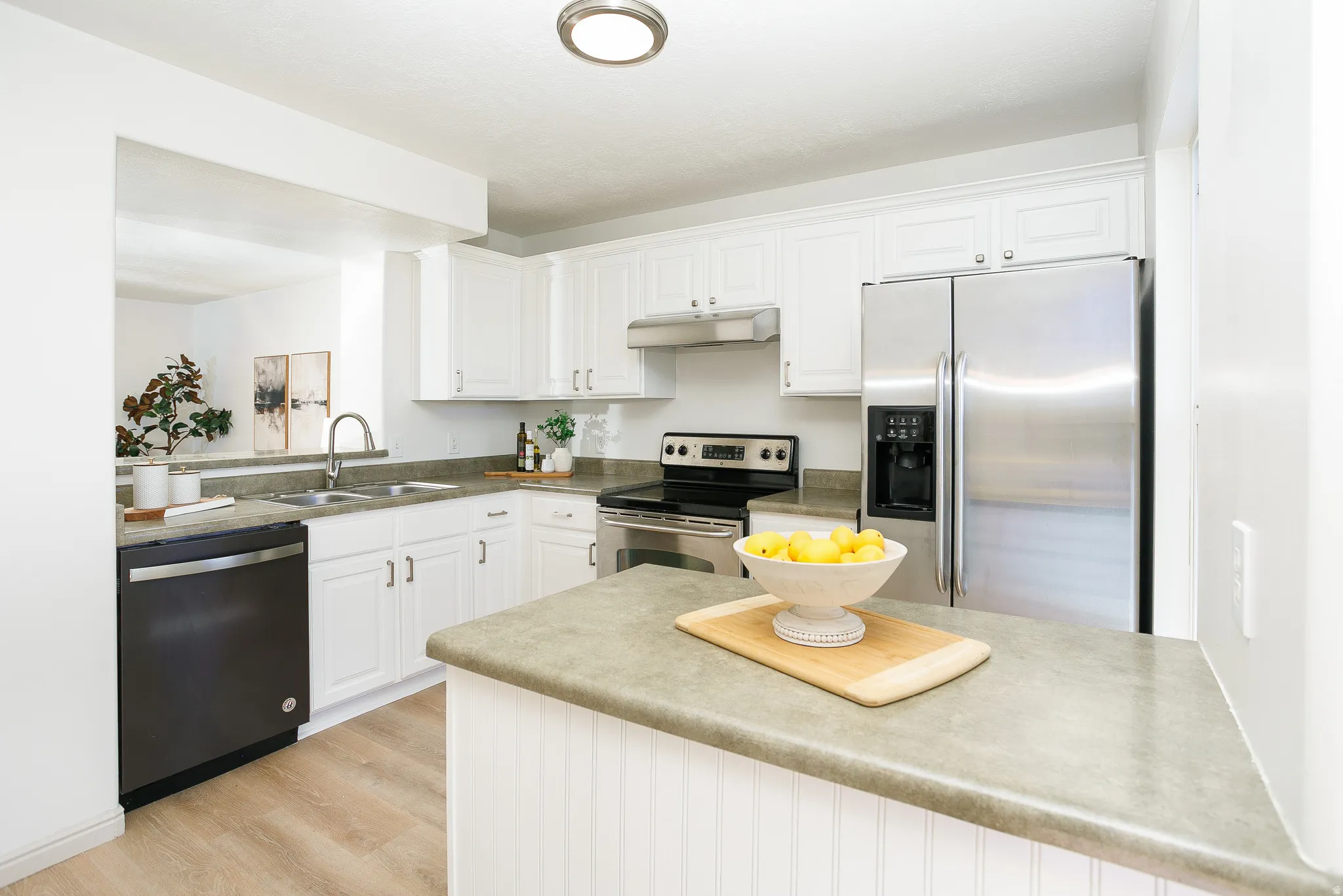 White cabinetry, stainless steel appliances, dual basin sink, wood-finish flooring, and a breakfast bar