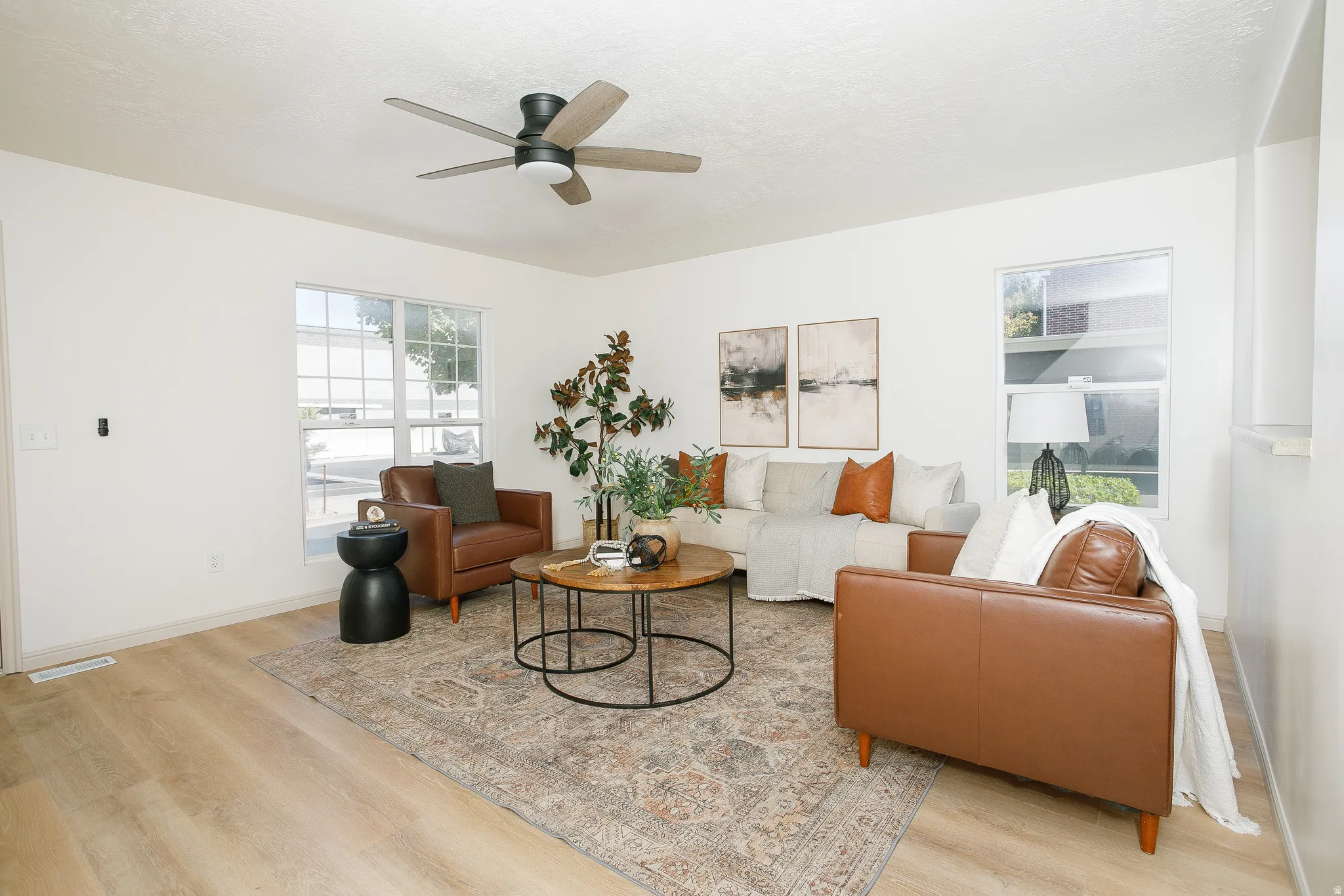 Wood-finish flooring, white walls, multiple windows, and a ceiling fan with integrated lighting