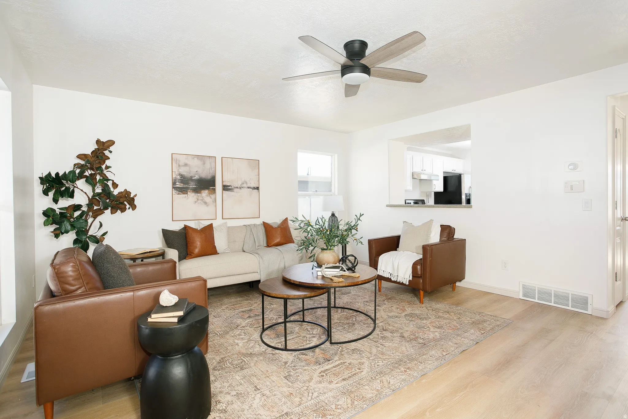 Light wood-finish flooring, a ceiling fan with light fixture, and a pass-through window to the kitchen