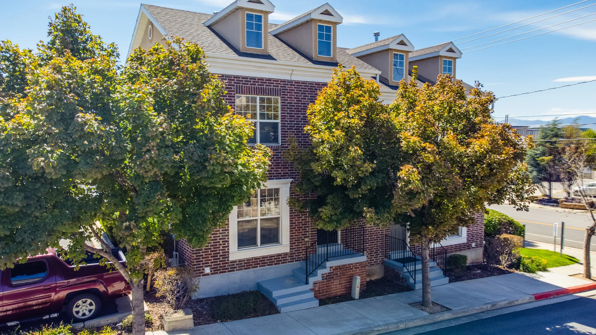 Brick facade with white trim, multiple dormer windows, a pitched roof, and mature trees