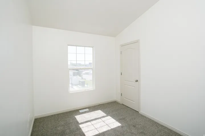 Carpeted flooring, white interior door, window with grid, white walls, vaulted ceiling