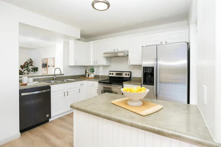 White cabinetry, stainless steel appliances, dual basin sink, wood-finish flooring, and a breakfast bar