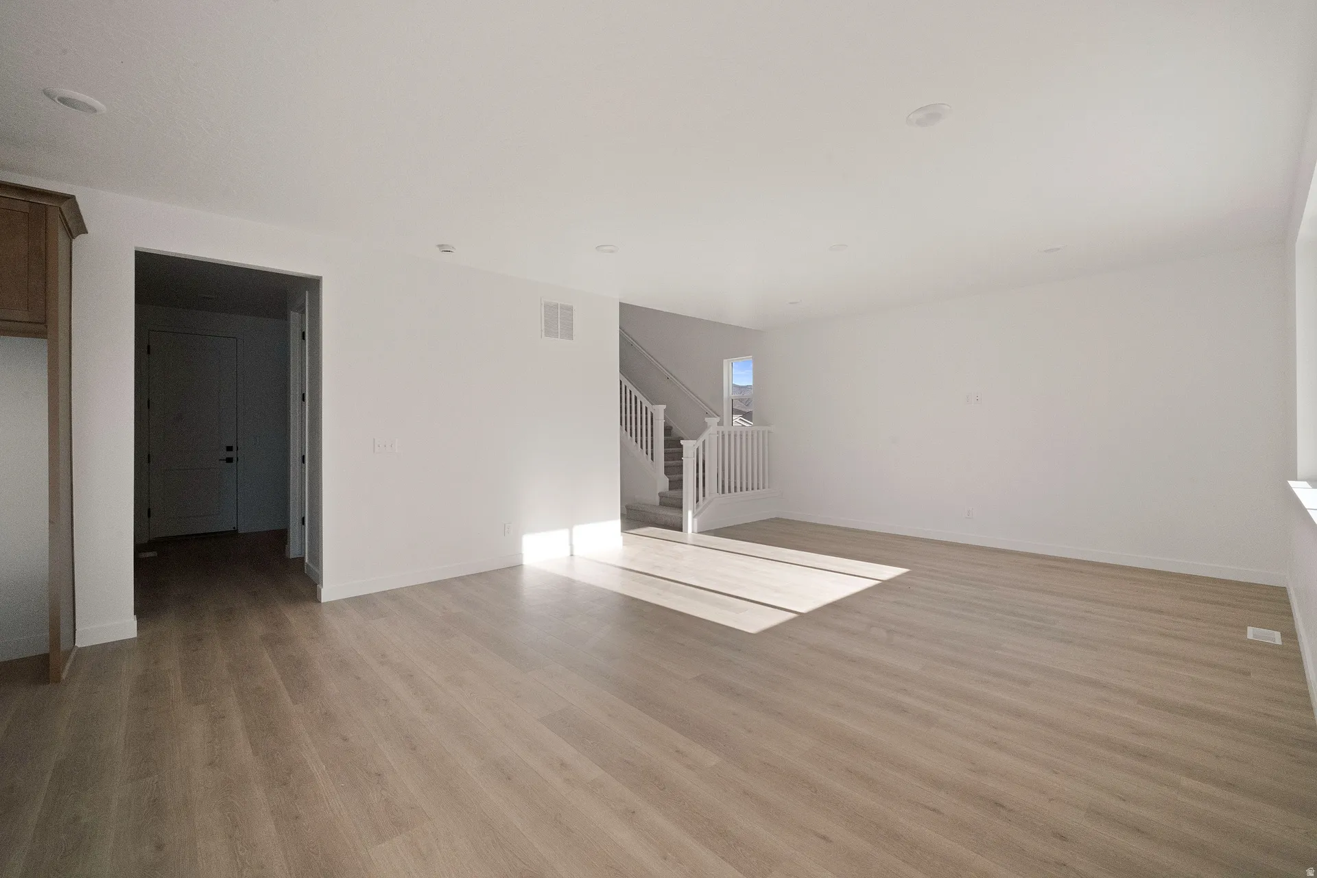 Spacious room with wood-finish flooring, recessed lighting, and a white staircase with balusters