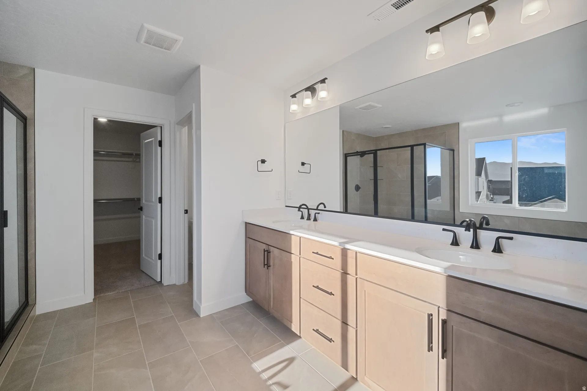 Dual vanity with undermount sinks, tile flooring, walk-in shower with glass enclosure, and a walk-in closet