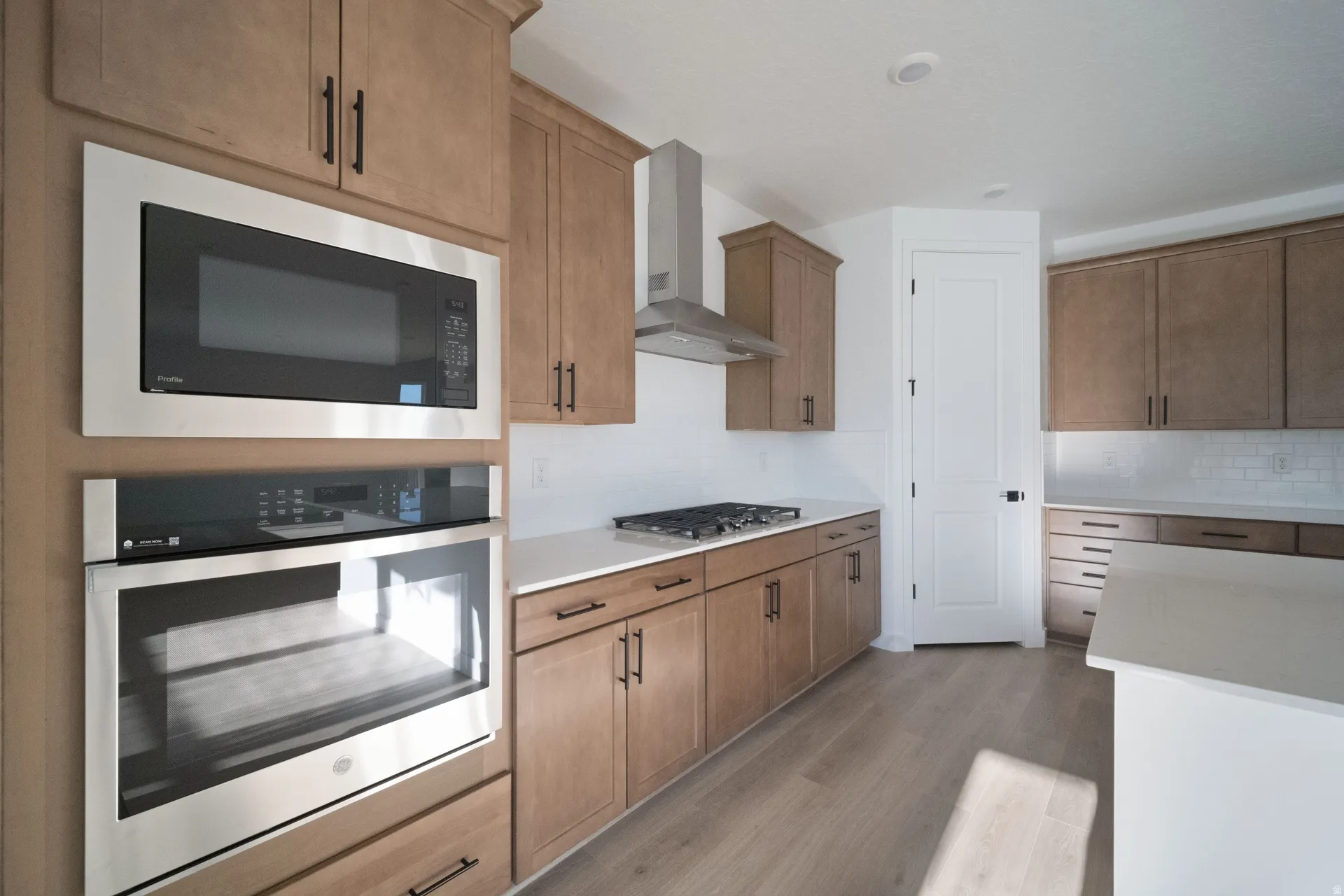 Kitchen featuring wood-finish cabinetry, stainless steel appliances, white countertops, a gas range with a stainless steel hood, and subway tile backsplash