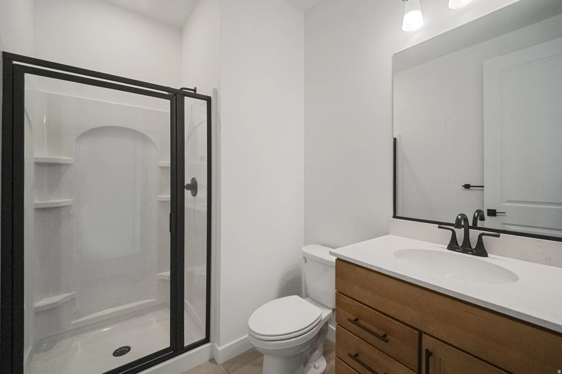 Black-framed shower enclosure, wood-finish vanity with drawer storage, white countertop with integrated sink, matte black faucet, and rectangular mirror