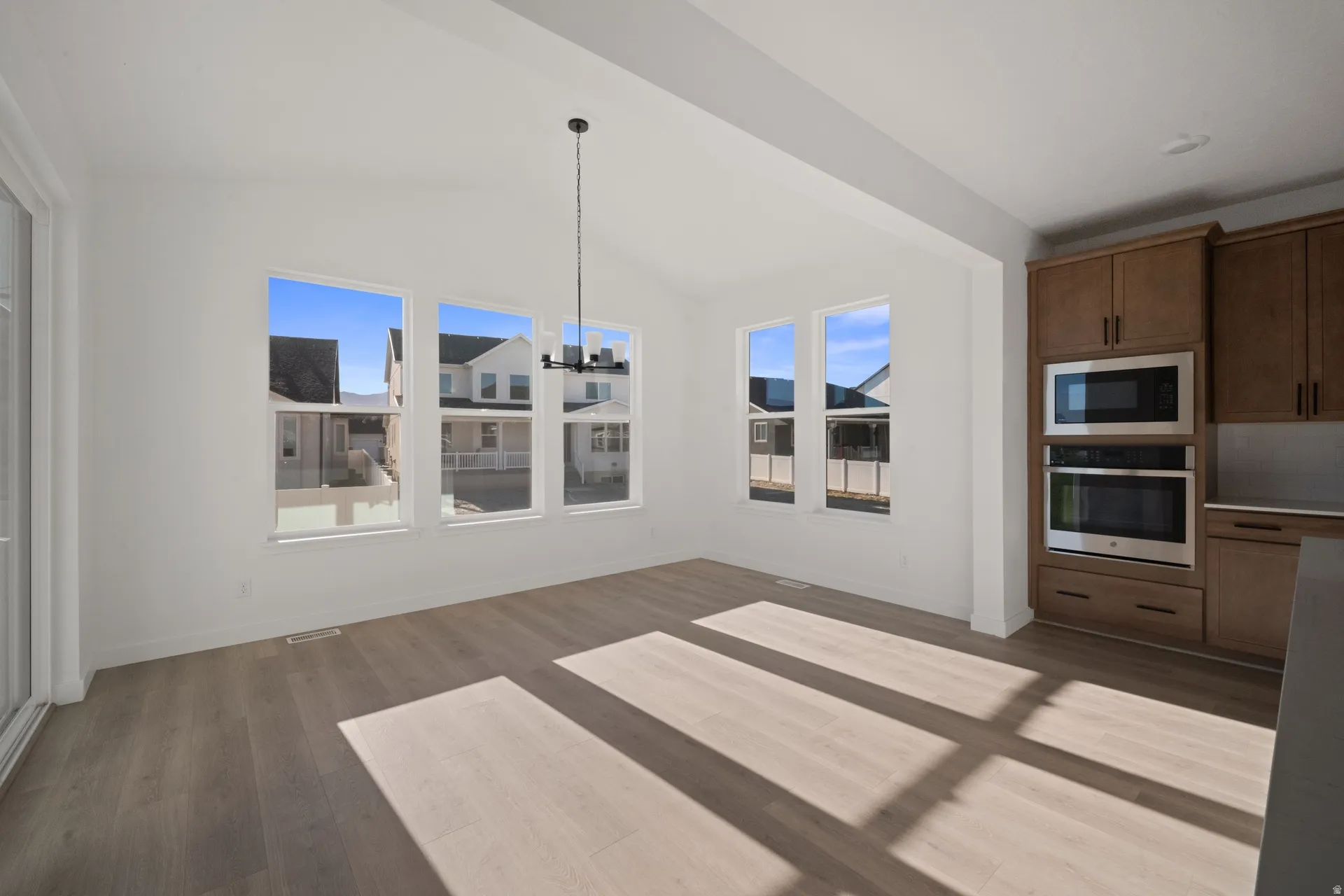Vaulted ceiling with a chandelier, wood-finish flooring, multiple windows, built-in microwave, and built-in oven