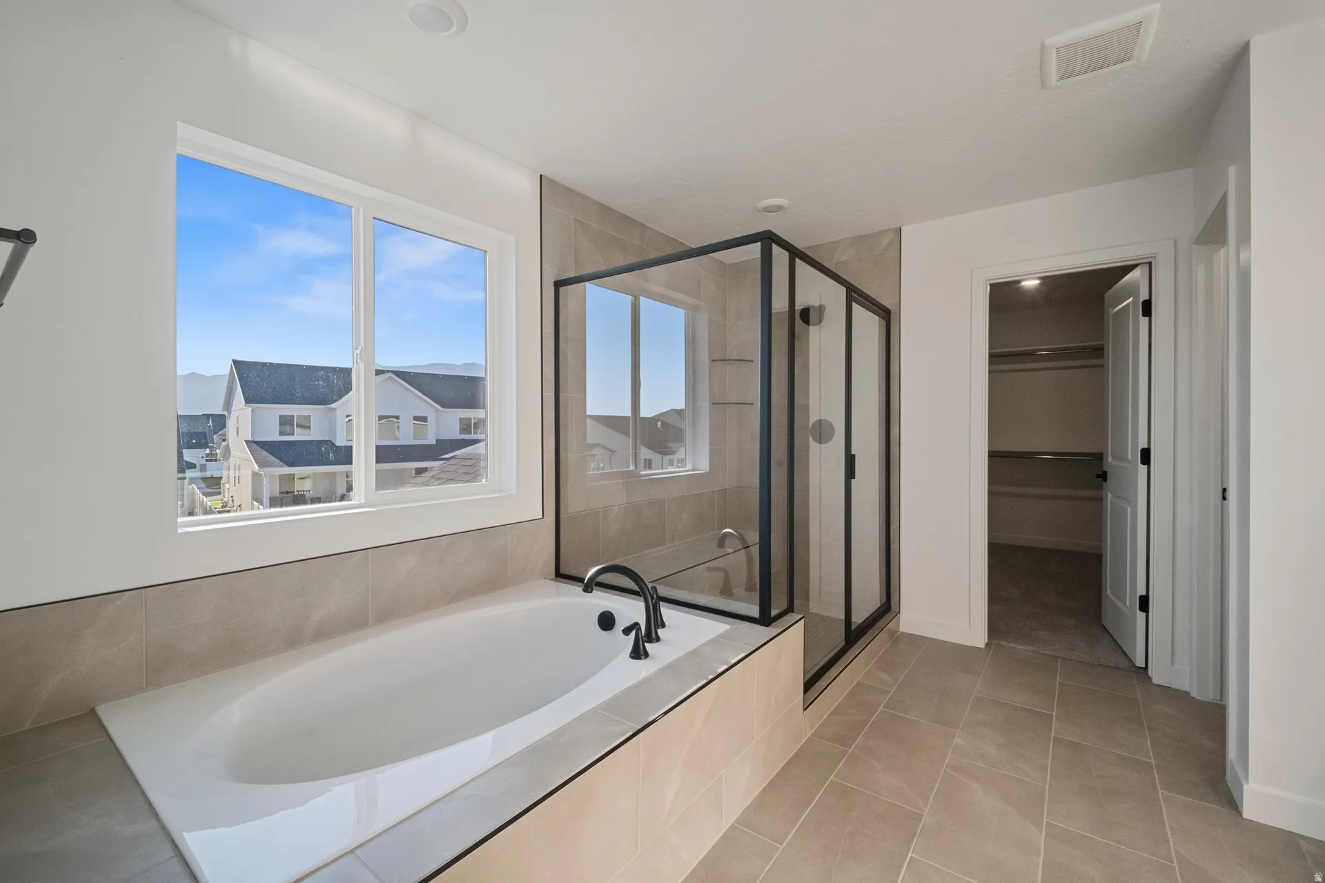 Soaking tub with a matte black faucet, glass-enclosed shower with black framing, and large format tiled flooring