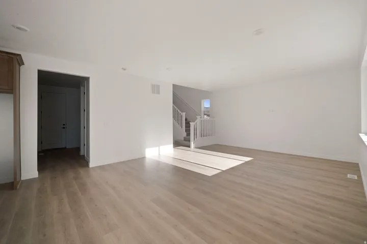 Spacious room with wood-finish flooring, recessed lighting, and a white staircase with balusters