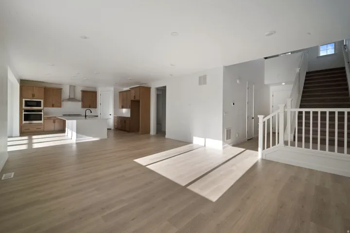 Open-concept living space featuring wood-finish flooring, recessed lighting, a kitchen island, double ovens, and a staircase with white balusters