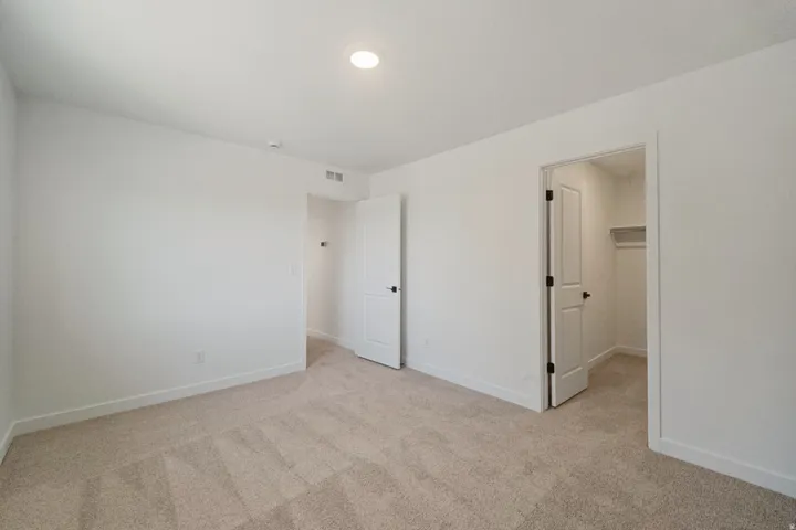 Plush carpet flooring, recessed ceiling lighting, crisp white walls, and a convenient closet with shelving