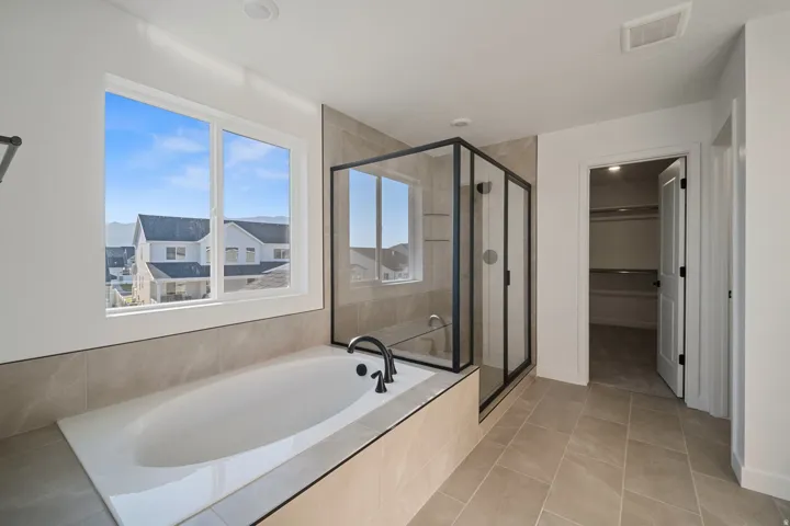 Soaking tub with a matte black faucet, glass-enclosed shower with black framing, and large format tiled flooring
