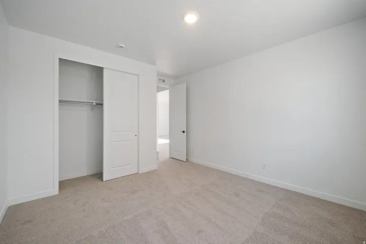 Recessed ceiling lighting, white interior walls, light-toned carpet flooring, white sliding closet doors, and a built-in closet rod