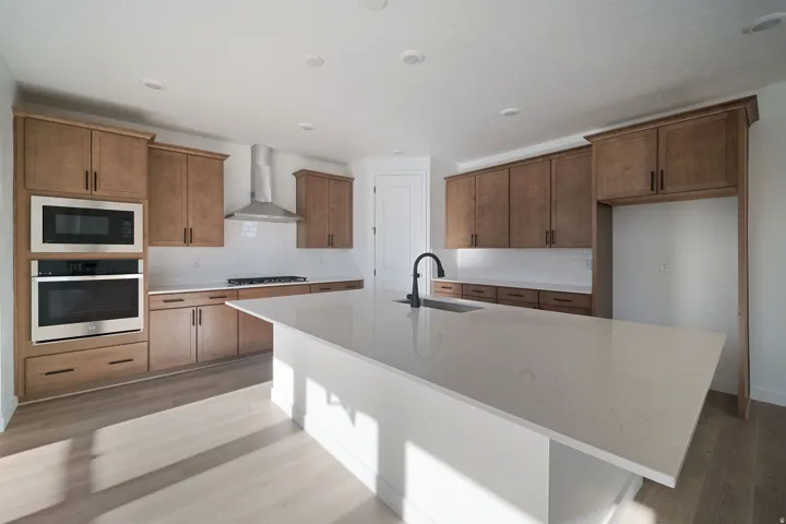 Kitchen with wood cabinetry, stainless steel appliances, white subway tile backsplash, white countertop island, and wood-finish flooring