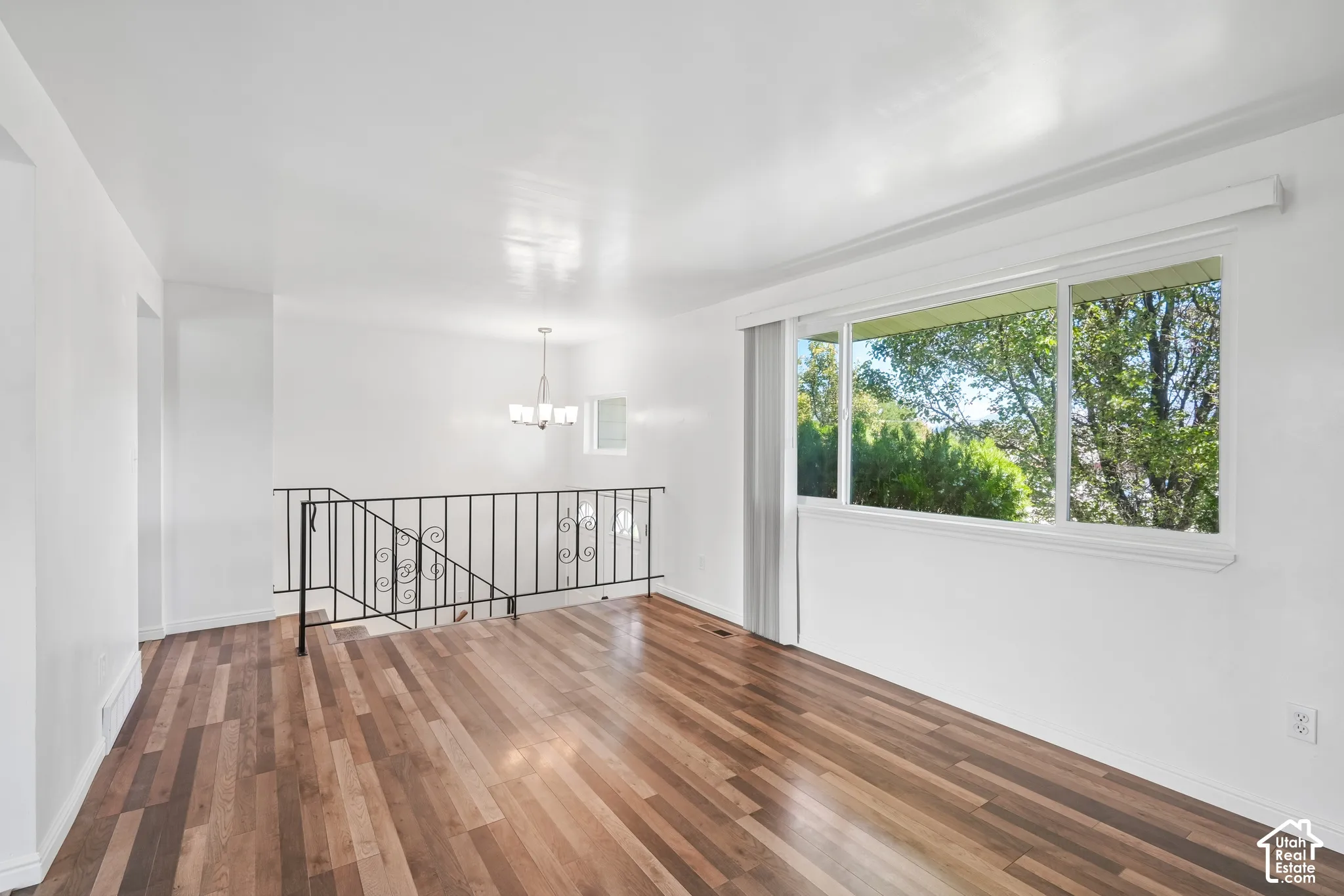 Wood-finish flooring, white walls, large multi-pane window, decorative wrought iron railing, and a contemporary chandelier