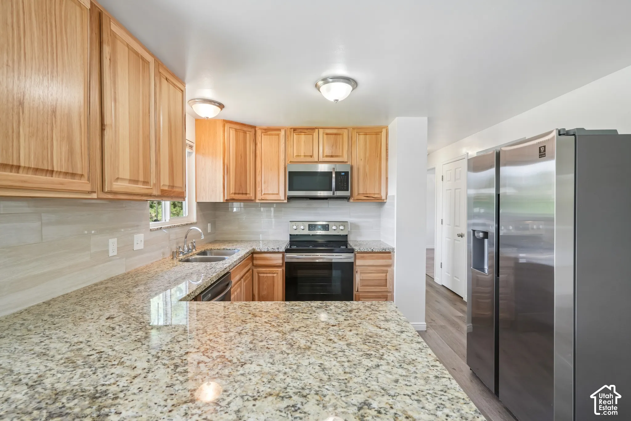Kitchen featuring granite countertops, wood cabinetry, tile backsplash, stainless steel appliances, and wood-finish flooring