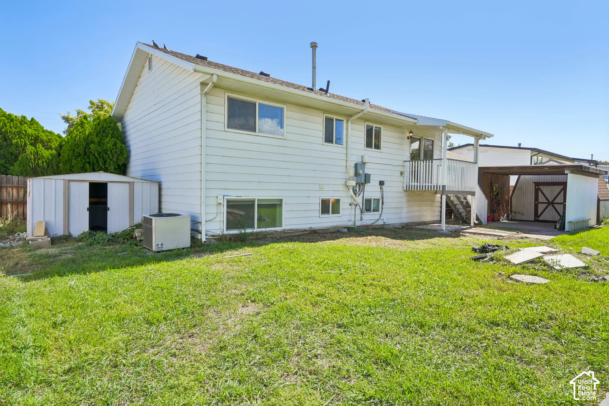 Rear exterior with white siding, upper-level deck, and two storage sheds