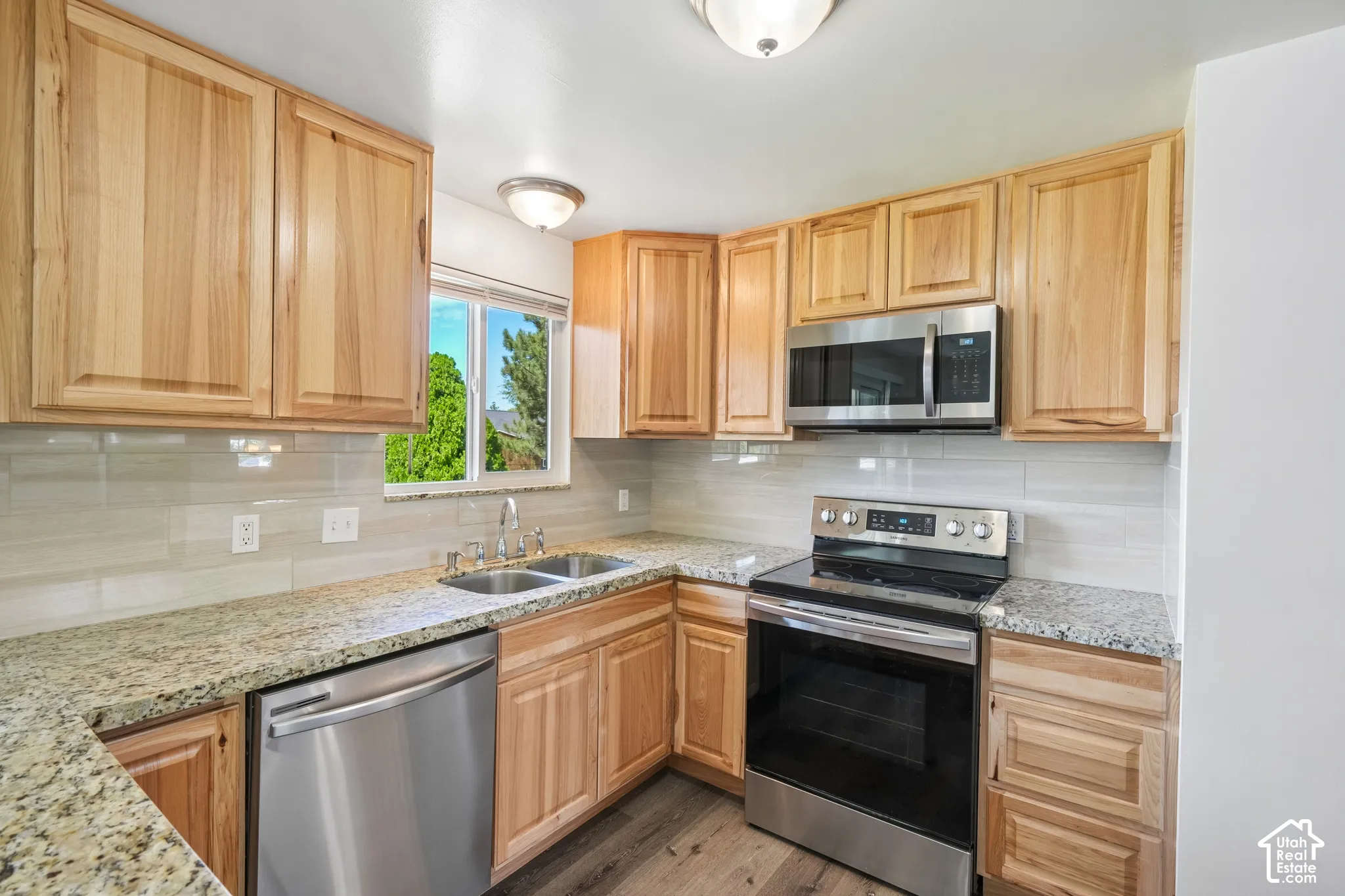 Wood-finish cabinetry, stainless steel appliances, granite countertops, tile backsplash, and wood-finish flooring